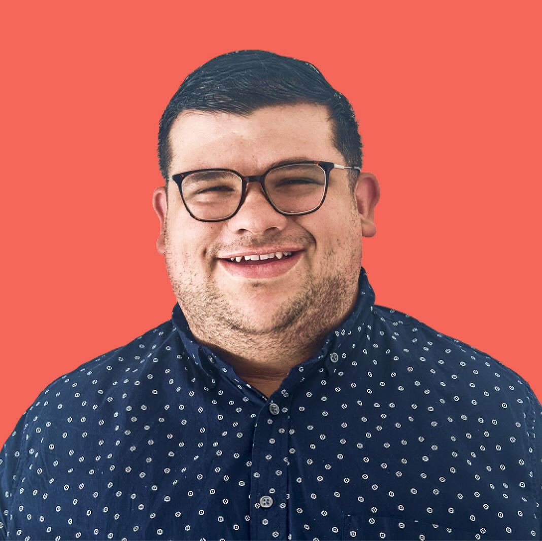 Roberto Perez, smiling, in a navy patterned shirt against a coral background
